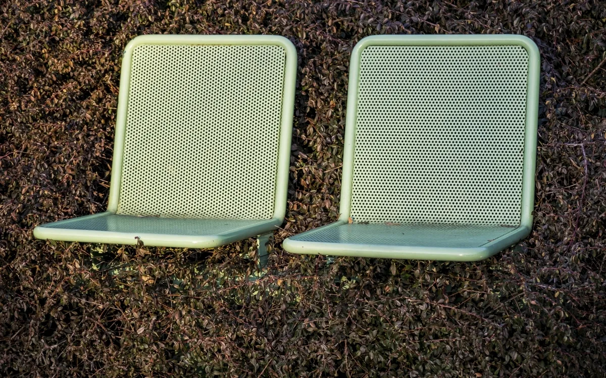 Two pale green perforated seats mounted against a dry hedge